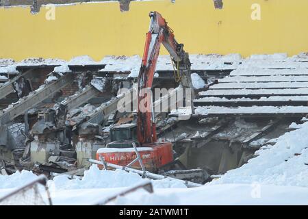 Ein Bagger mit einem Jackhammer zerstört im Winter ein Betongebäude. Baumaschinen. Stockfoto