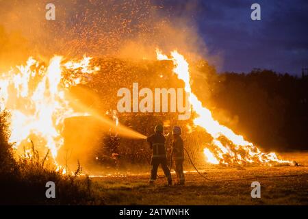 Zwei Feuerwehrleute zünden Heuhaufen in Perry Green, Much Hadham, Hertfordshire. GROSSBRITANNIEN Stockfoto