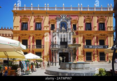 Steinbrunnen auf dem Obispo-Platz mit dem Bischofspalast nach hinten und Menschen, die sich in Straßencafés, Málaga, Spanien entspannen. Stockfoto