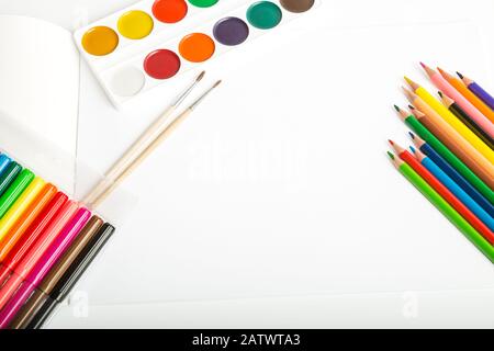 Auf dem leeren Blatt zum Zeichnen liegen farbige Bleistifte, Filzstifte, Aquarellfarben und Bürsten auf weißem Hintergrund, Kopierraum für Text Stockfoto