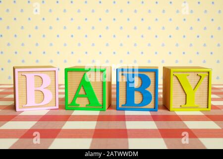 Baby, Wort. Kinderhölzerne ABC-Buchstabenalphabetblöcke buchstabieren BABY auf einer karierten Tischdecke Stockfoto