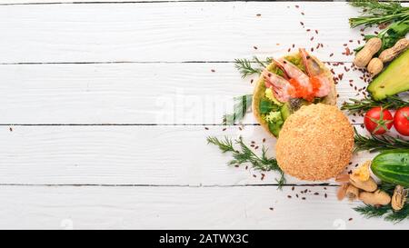 Burger, Sandwich mit Garnelen, Avocado, Kaviar und Gurke. Auf Holzgrund. Draufsicht. Kopierbereich. Stockfoto