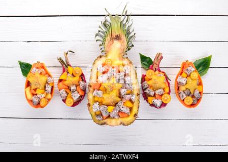 Exotischer Obstsalat in einer halben Ananas. Papaya, Drachenfrucht, Tamarind, Kakteenobst, Mango, Mangosteen Auf Holzgrund. Draufsicht. Stockfoto