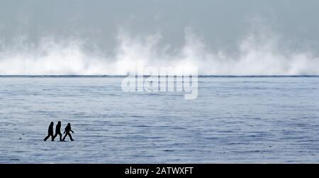 Silhouette von drei Personen, die an einem eisigen, kalten sonnigen Tag auf einem großen gefrorenen Fluss spazieren gehen Stockfoto