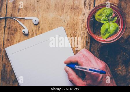 Minimaler Arbeitsbereich mit leerem Notizblock, Stift, Ohrhörer und Glas Wasser mit Minzblättern auf einem alten Holzschreibtisch. Retro-Konzept. Stockfoto