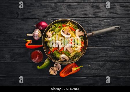 Nudeln mit Gemüse in einer Pfanne. Asiatische Küche Pasta. Draufsicht. Freier Speicherplatz. Auf einem Holzhintergrund.; Stockfoto