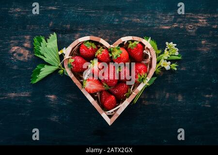 Erdbeeren in einer Kiste in Form eines Herzens. Auf Holzgrund. Draufsicht. Kopierbereich. Stockfoto