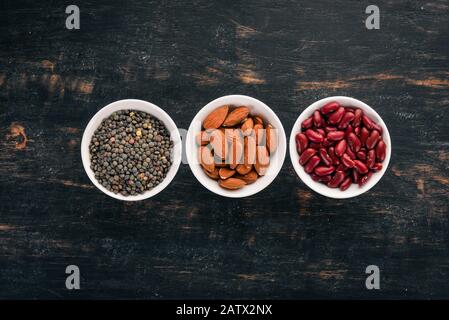 Linsen, Mandeln und Bohnen. Auf schwarzem Holzhintergrund. Draufsicht. Freier Speicherplatz. Stockfoto