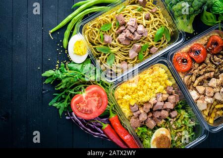 Pasta und Buchweizen mit Fleisch und frischem Gemüse. Gesunde Ernährung Essen. Mittagsboxen. Auf schwarzem Holzhintergrund. Draufsicht. Freier Speicherplatz für Text. Stockfoto