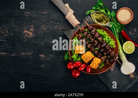 Spieße von Hühnerherzen, Mais und frischem Gemüse. Auf Holzgrund. Draufsicht. Freier Speicherplatz. Stockfoto