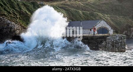 Stürmische Meere krachen gegen die steinernen Hafenmauern, die das Bootshaus in Ballintoy schützen Stockfoto