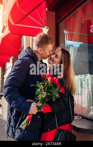 Valentinstagspaar küsst sich. Der Mann, der der Freundin auf dem heutigen Tag rote Rosen-Blumen im Café in der Stadt schenkt. Frauentag Stockfoto