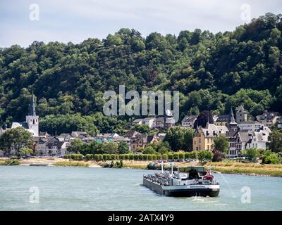 SANKT GOAR, DEUTSCHLAND - 06. JULI 2019: Frachtschiff auf dem Rhein mit dem Dorf St. Goar im Hintergrund Stockfoto