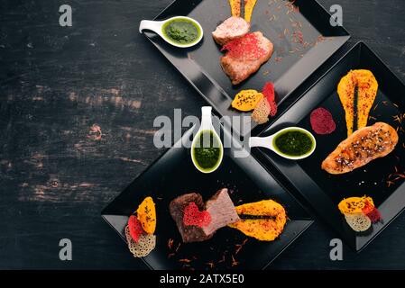 Auswahl an Fleischgerichten. Hühnerfleisch, Kalbfleisch und Schweinefleisch mit Sauce. Auf Holzgrund. Freier Speicherplatz für Text. Draufsicht. Stockfoto