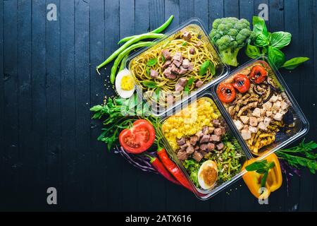 Pasta und Buchweizen mit Fleisch und frischem Gemüse. Gesunde Ernährung Essen. Mittagsboxen. Auf schwarzem Holzhintergrund. Draufsicht. Freier Speicherplatz für Text. Stockfoto