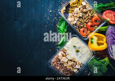 Pasta und Buchweizen mit Fleisch und frischem Gemüse. Gesunde Ernährung Essen. Mittagsboxen. Auf schwarzem Holzhintergrund. Draufsicht. Freier Speicherplatz für Text. Stockfoto