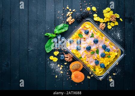 Haferflocken mit Blaubeeren und Joghurt. Gesunde Ernährung. Lunchboxen. Auf schwarzem Holzhintergrund. Draufsicht. Freier Speicherplatz für Text. Stockfoto