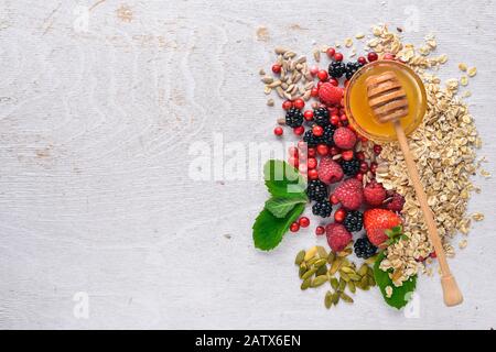 Gesunde Ernährung. Frische Wildbeeren, Kupfer, Nüsse, Haferbrei, Trockenfrüchte und Samen. Auf Holzgrund. Draufsicht. Freier Speicherplatz für Text. Stockfoto
