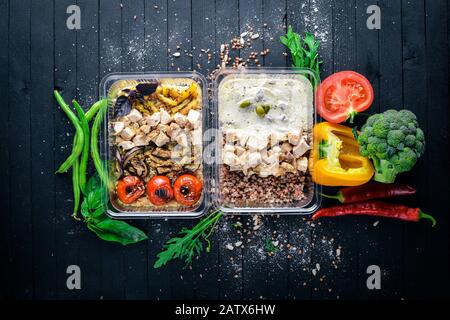 Pasta und Buchweizen mit Fleisch und frischem Gemüse. Gesunde Ernährung Essen. Mittagsboxen. Auf schwarzem Holzhintergrund. Draufsicht. Freier Speicherplatz für Text. Stockfoto