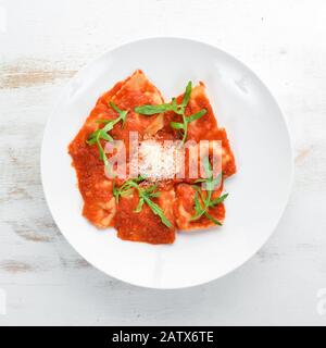 Klassische Ravioli mit Tomatensauce und Parmesankäse. Italienische Küche. Knödel. In einer Platte auf Holzhintergrund. Draufsicht. Freier Speicherplatz. Stockfoto
