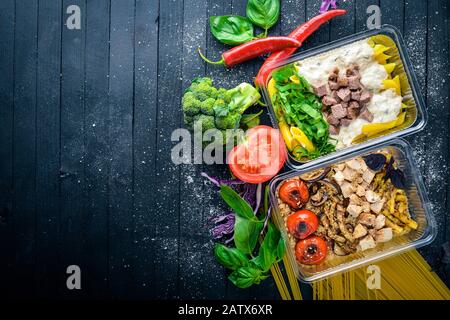 Pasta und Buchweizen mit Fleisch und frischem Gemüse. Gesunde Ernährung Essen. Mittagsboxen. Auf schwarzem Holzhintergrund. Draufsicht. Freier Speicherplatz für Text. Stockfoto