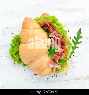 Sandwich mit Scheiben Prosciutto auf altem Holzhintergrund. Croissant Frühstück. Draufsicht. Freier Speicherplatz für Ihren Text. Stockfoto