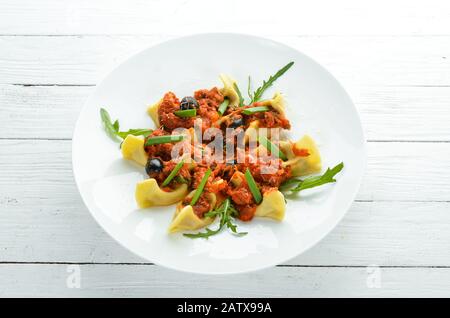 Ravioli mit Fleisch- und Tomatensauce und Oliven. In einer Platte auf Holzhintergrund. Draufsicht. Freier Speicherplatz. Stockfoto