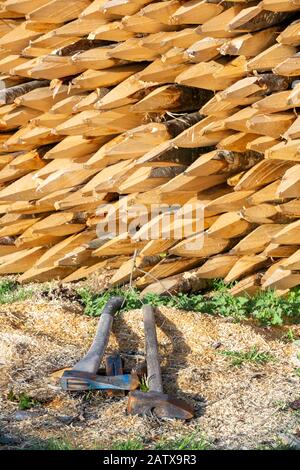 Manuell gehackte Holzpfosten mit spitzen Enden, die zum Fechten verwendet werden, wobei zwei Holzhackachsen auf dem Boden liegen. Stockfoto