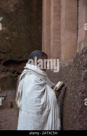 Lalibela, Äthiopien - November 2018: Mann in weiße traditionelle äthiopische Kleidung gekleidet, die an der ausgegrabenen Felsenkirchenkirche in Lalibela bettet. Stockfoto