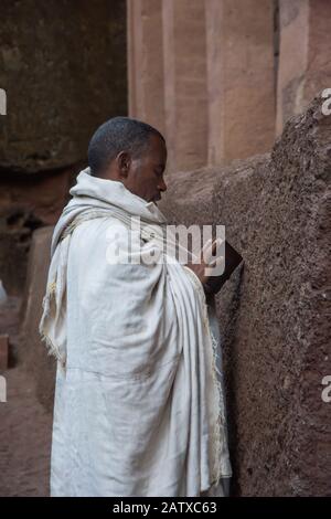 Lalibela, Äthiopien - November 2018: Mann in weiße traditionelle äthiopische Kleidung gekleidet, die an der ausgegrabenen Felsenkirchenkirche in Lalibela bettet. Stockfoto