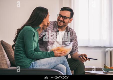 Ein glückliches Liebespaar erholt sich zu Hause. Sie beobachten fernsehen und essen Chips. Stockfoto