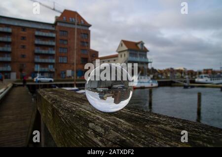 Lensball, Blick in die Kristallkugel am Hafen. Der Fischaugen-Effekt mit invertierter Perspektive liefert ein abstraktes Bild. Im Hintergrund verschwommene Schiff und po Stockfoto