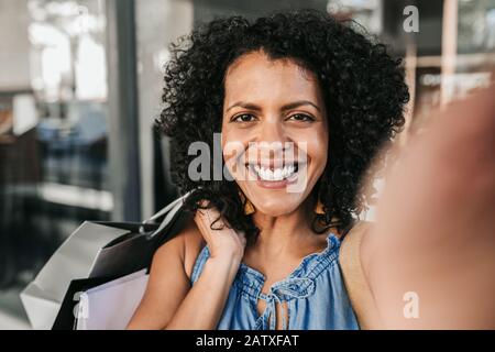 Junge Frau lächelt und nimmt selfie beim Einkaufen Stockfoto