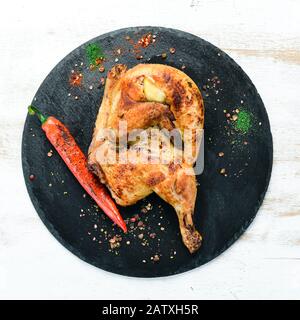 Gebackene Wachtel, Huhn mit Chili Pfeffer auf einem schwarzen Steinteller. Draufsicht: Freier Speicherplatz für Ihren Text. Rustikaler Stil. Stockfoto