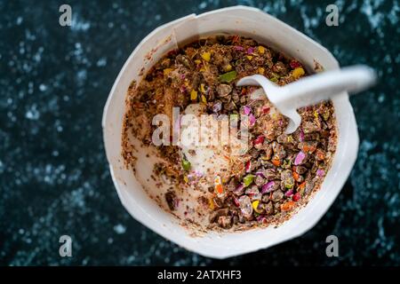 Nehmen Sie Eiscreme mit Süßigkeiten, Bonbon und Schokoladenstückchen in Plastikbecher mit Löffel weg. Bereit zum Essen. Stockfoto