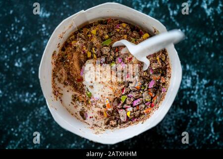 Nehmen Sie Eiscreme mit Süßigkeiten, Bonbon und Schokoladenstückchen in Plastikbecher mit Löffel weg. Bereit zum Essen. Stockfoto