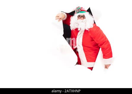 Weihnachtsmann aus einem Loch in Papier. Weihnachtsfeiertage. Mann in einem Neujahrsanzug von der Wand Stockfoto