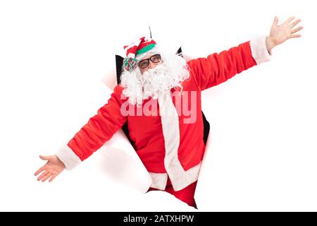 Weihnachtsmann aus einem Loch in Papier. Weihnachtsfeiertage. Mann in einem Neujahrsanzug von der Wand Stockfoto