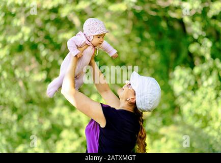 Glückliche Mutter wirft Baby in der Natur auf unscharfen Hintergrund Stockfoto