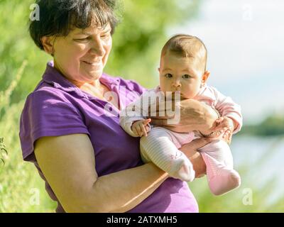 Baby-Mädchen an den Händen ihrer Großmutter in der Natur Stockfoto