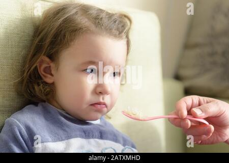Kind weigert sich zu essen. Das dreijährige Kind wird zuhause mit einem Löffel gefüttert. Süße Baby-Mädchen trauern, weil sie das Essen nicht mag. Porträt von Finn Stockfoto