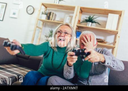 Älteres Paar hat Spaß zu Hause Videospiel mit Joysticks in den Händen. Stockfoto