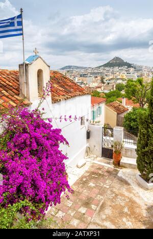 Alte Kirche in Anafiotika, Stadtteil Plaka, Athen, Griechenland. Plaka ist eine der wichtigsten Touristenattraktionen Athens. Landschaftlich reizvolles Haus mit einer griechischen Flagge an der TH Stockfoto