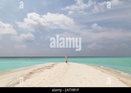 Konzept Reisen - Frau am Strand; EINE alleinstehende Frau, die an einem tropischen Strand mit weißem Sand, blauem Himmel und türkisfarbenem Wasser steht, Rückansicht, die Malediven, Asien Stockfoto