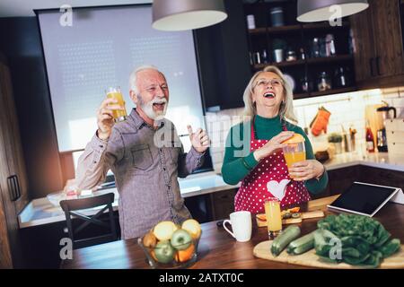 Das schöne Senioren-Paar tanzt und lächelt beim gemeinsamen Kochen in der Küche Stockfoto