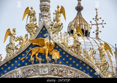 Engel und der Löwe auf der Spitze der Fassade der Markusbasilika (Markusdom) in Venedig, Italien. Der geflügelte Löwe ist ein Symbol Venedigs. Stockfoto