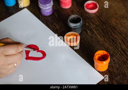 Auf weißem Papier erzeugen Gouache-Farben ein Herzmuster. Schulterschuss. Selektiver Fokus. Anordnung von Fotos im Querformat. Stockfoto