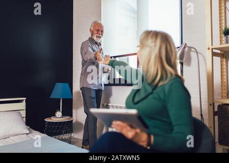 Älteres Paar im Schlafzimmer. Frau mit Tablette, Mann trinkt Wein. Stockfoto