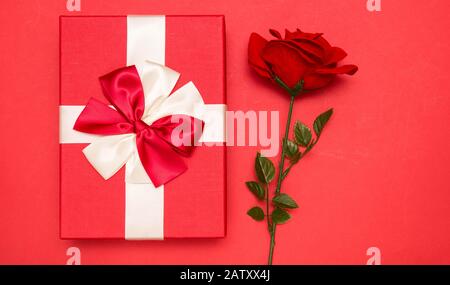 Echte Schachtel mit weißem und rotem Bogen mit Band und roter Rose, Draufsicht am Valentinstag isoliert auf rotem Hintergrund. Flaches Lay. Kopierbereich. Stockfoto