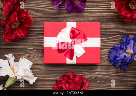 Echte Schachtel mit weißem und rotem Bogen und Band und verschiedenen Blumen Draufsicht am Valentinstag isoliert auf Holzhintergrund. Flaches Lay. Kopierbereich. Stockfoto